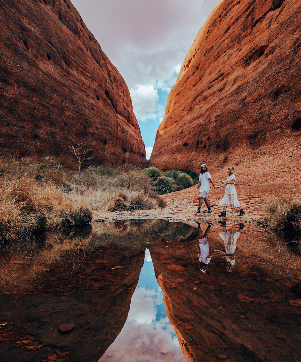 a young man and woman, dressed in white, hold hands walking through Walpa Gorge.