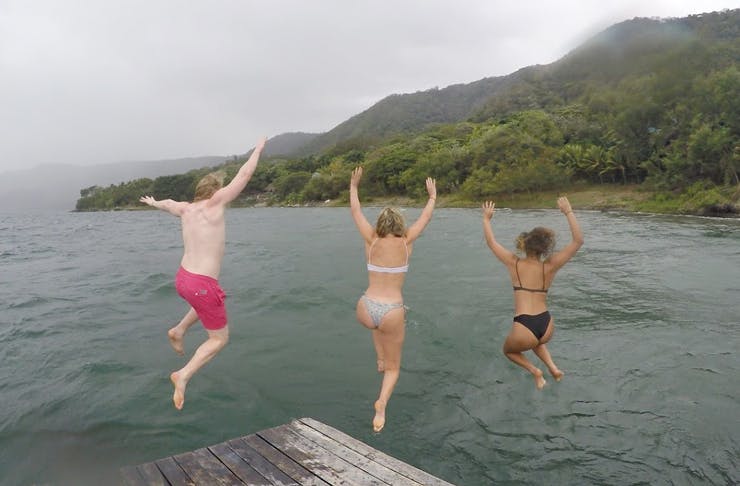 three people jumping off pontoon into a rainy lake