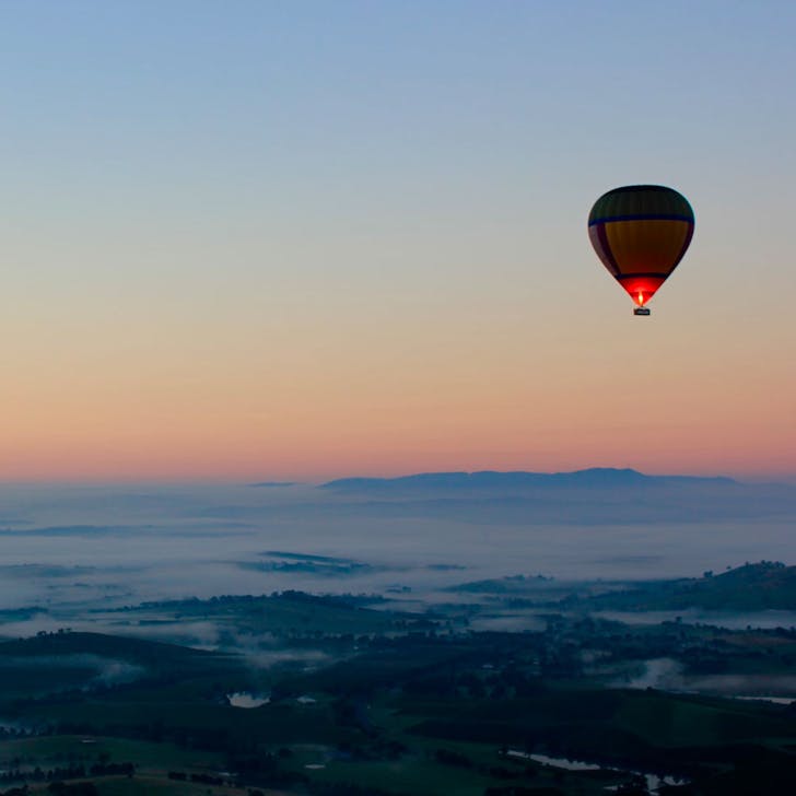 hot air balloon floating over a valley at sunrise