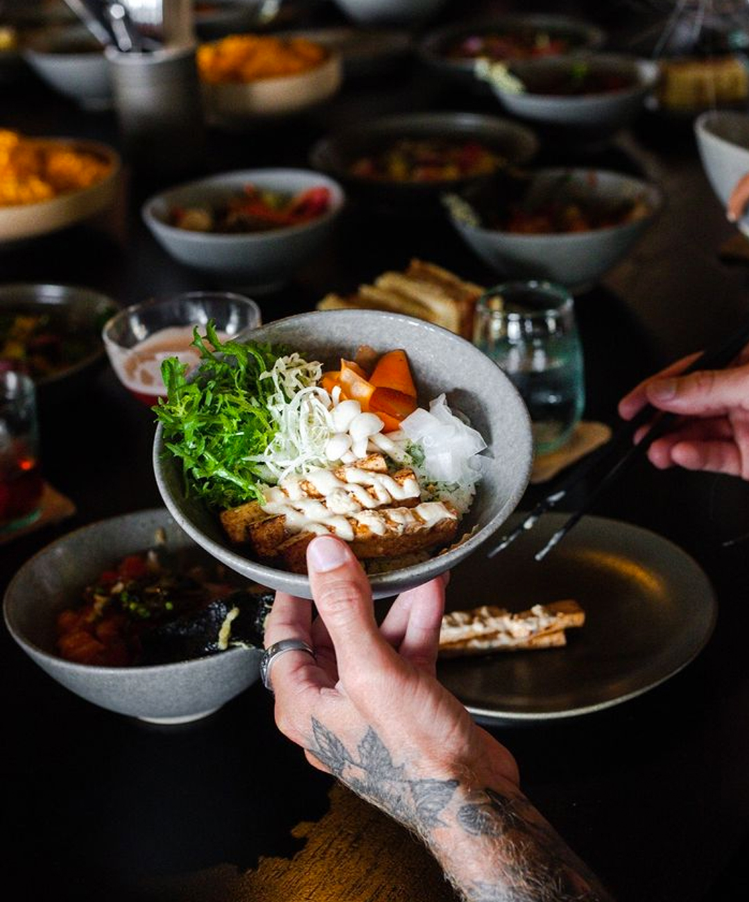 A tattooed hand holding up a bowl of vegetables and tofu