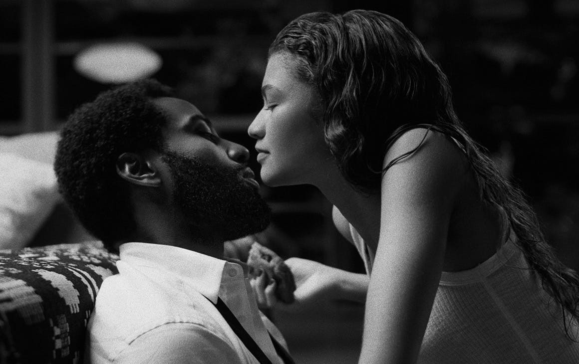 a black and white image of a young woman leaning in to a kiss a man on a couch.